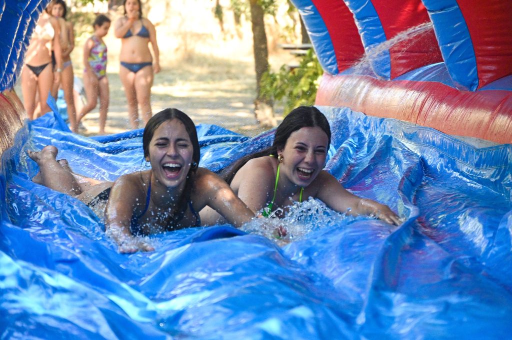 Dos chicas deslizándose por un tobogán acuático hinchable en el campamento de verano