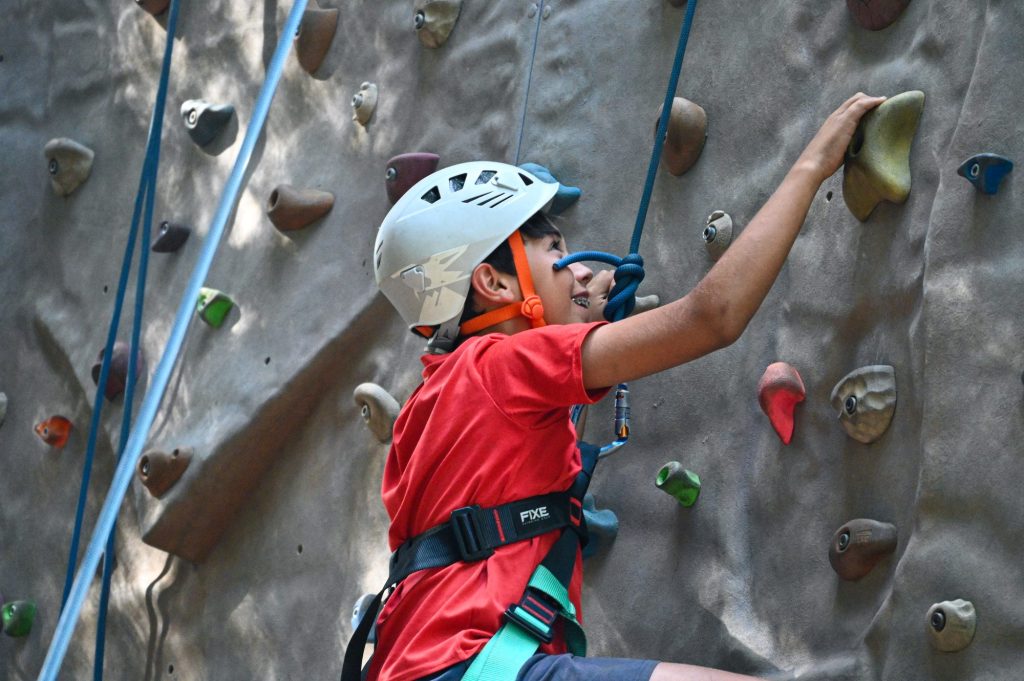 Chico escalando en el rocódromo con casco y arnés