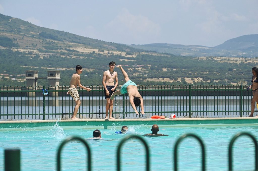Chicos saltando y bañándose en la piscina con el embalse al fondo
